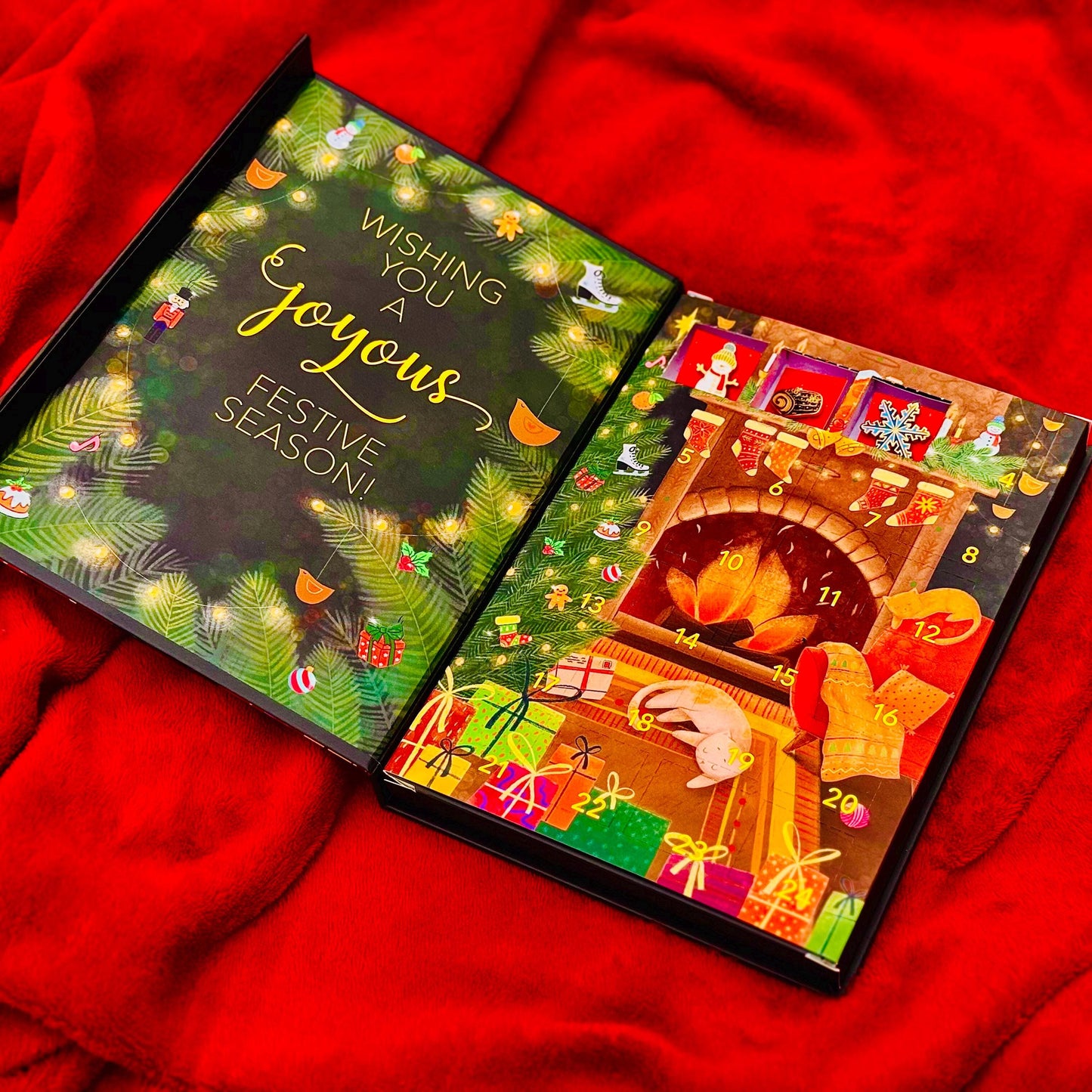 An open advent calendar with a festive design, featuring a fireplace, presents, and holiday decorations, all set against a red background.