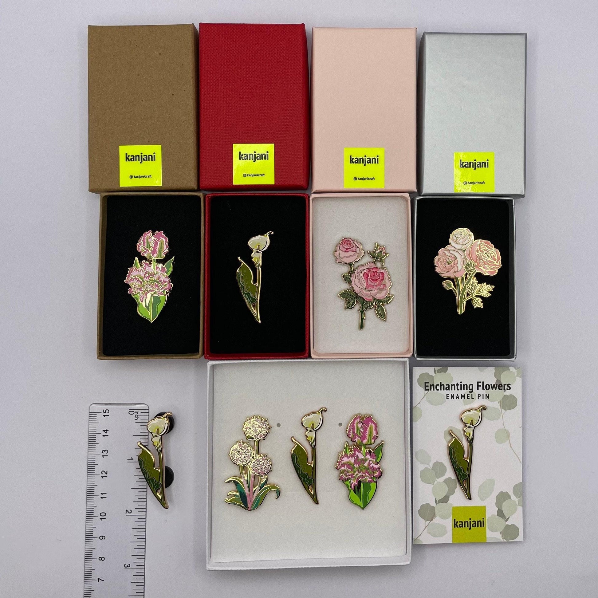 a collection of nine floral pin badges, each with a unique design, arranged in boxes and a ruler for size comparison.