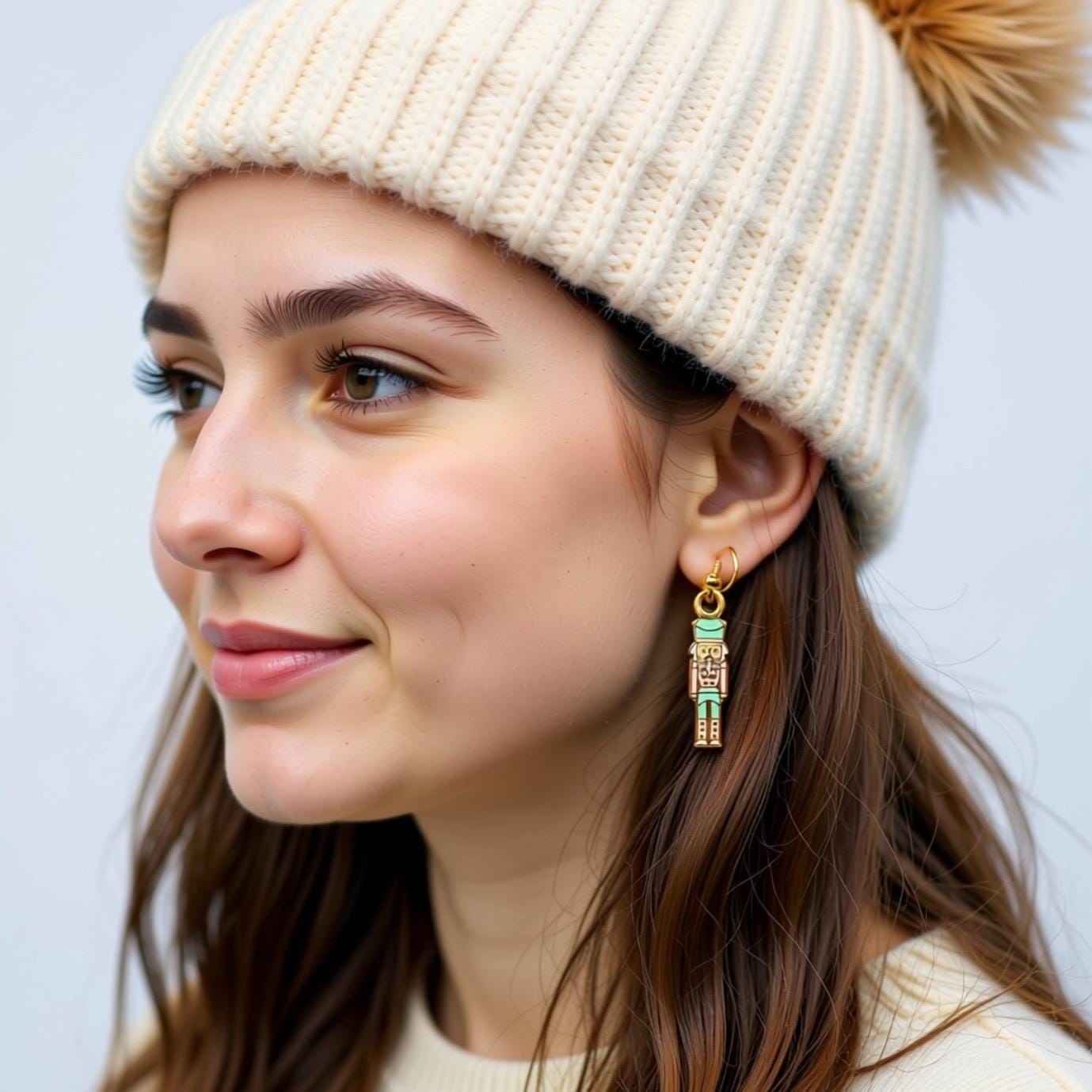 A woman wearing a white knit hat and earrings with a nutcracker design smiling at the camera.