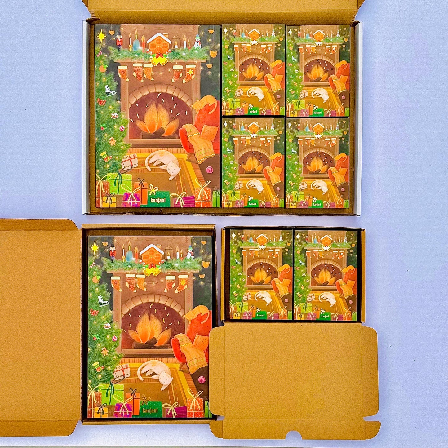 a set of Christmas-themed greeting cards displayed in a cardboard box. The cards feature illustrations of a fireplace, presents, and other holiday decorations, creating a festive atmosphere.