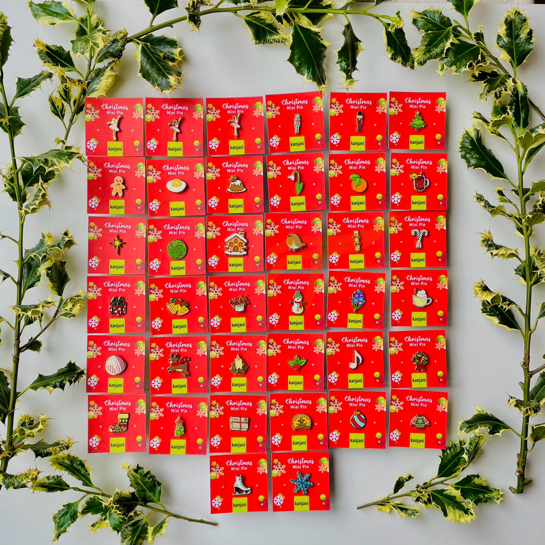 a collection of Christmas-themed pins arranged in a grid pattern on a white background. The pins are red and have various holiday-themed designs, such as Christmas trees, ornaments, and other festive elements. The pins are surrounded by green leaves, creating a festive and holiday atmosphere.