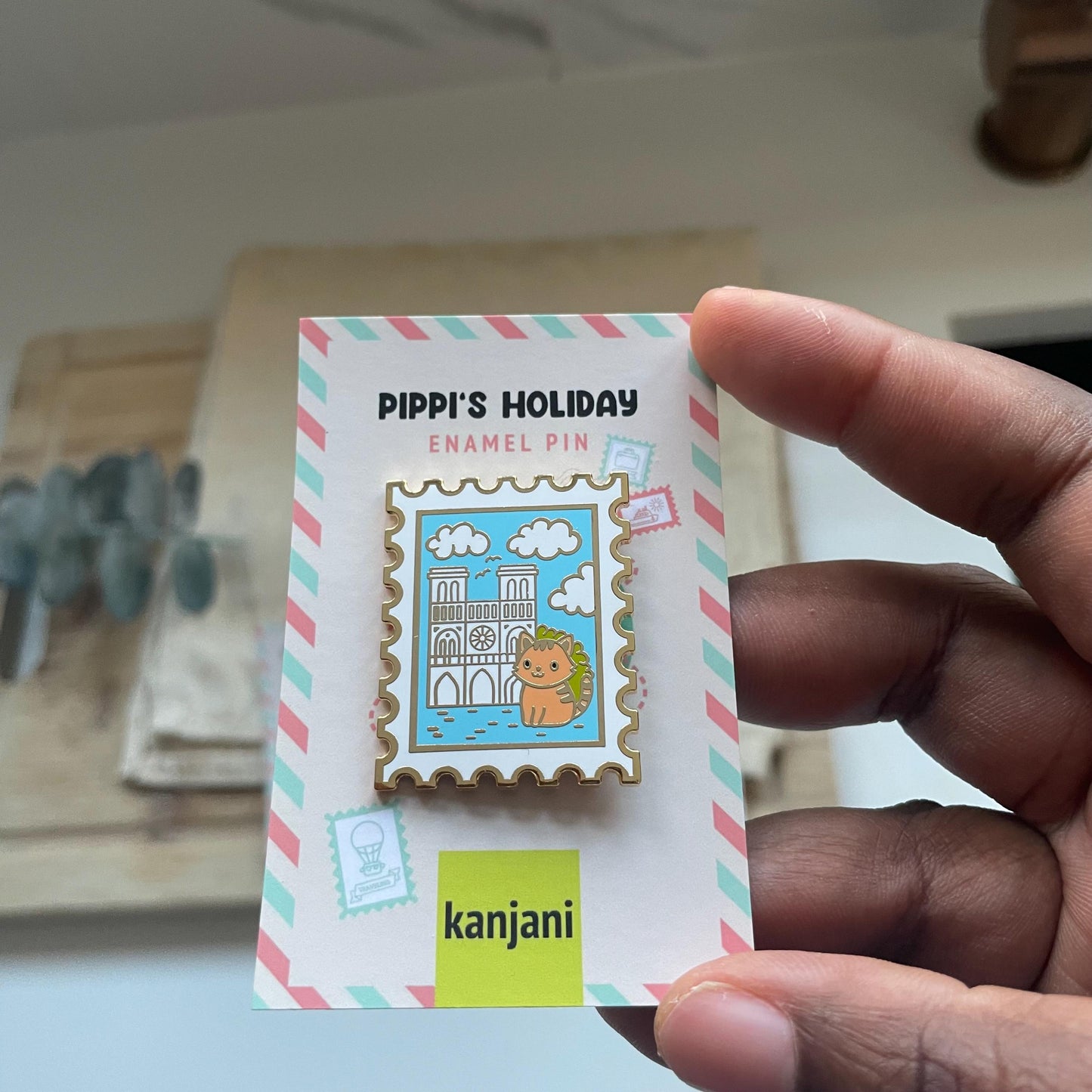 A hand is holding a colorful enamel pin featuring a cartoon character and a castle. The pin is labeled as "Pippi's Holiday" and is part of a "kanji" collection.