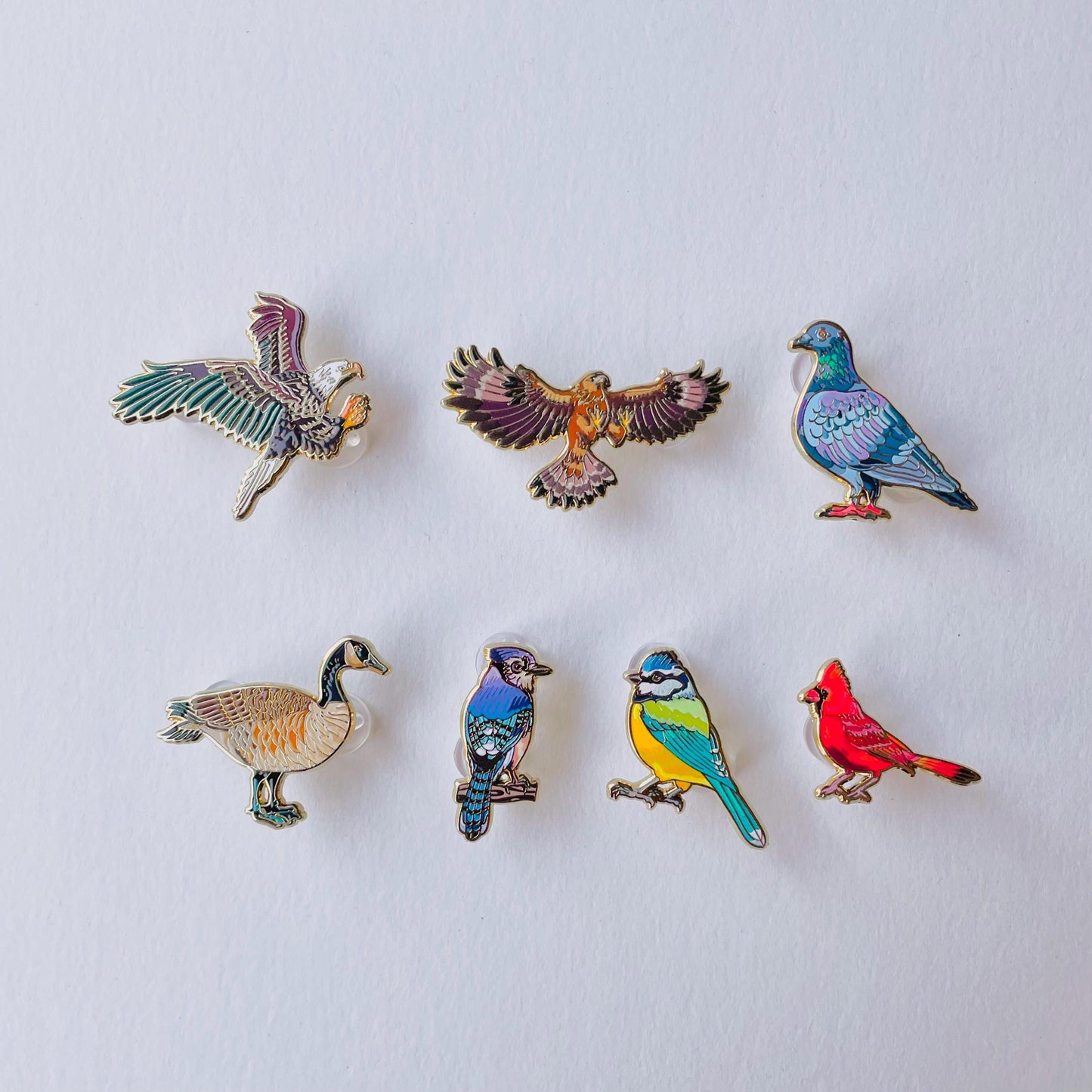 a collection of six bird pins, each with a unique design and color, arranged in a grid pattern on a white background.