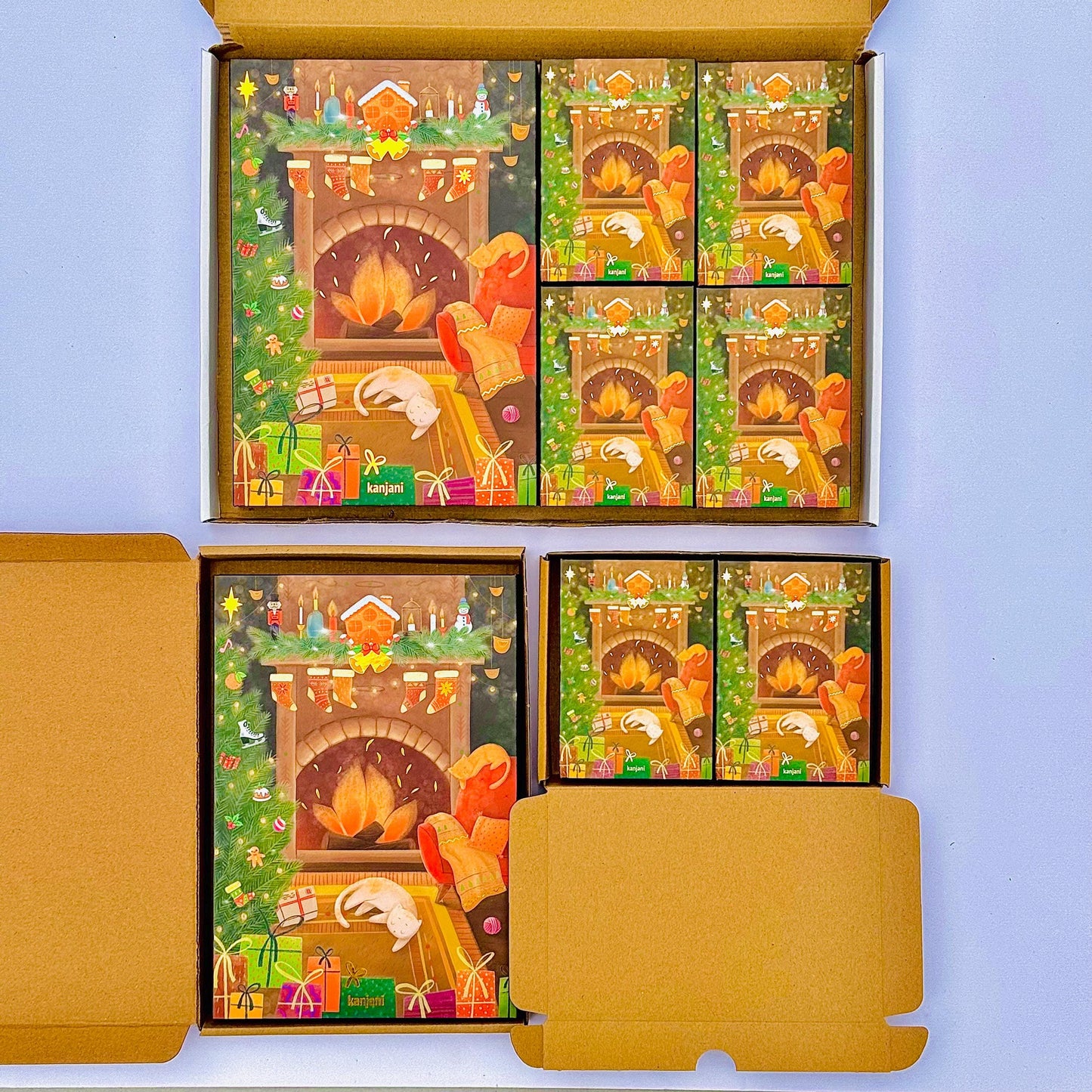 a set of Christmas-themed greeting cards displayed in a cardboard box. The cards feature illustrations of a fireplace, presents, and other holiday decorations, creating a festive atmosphere.