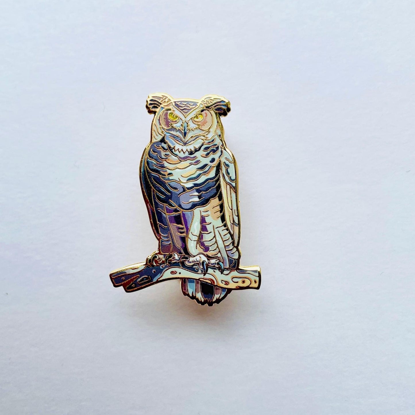 An ornate pin depicting an owl, with intricate details and a metallic finish.
