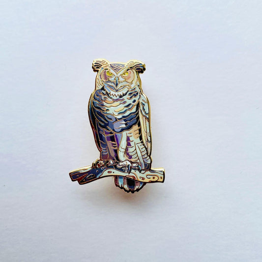 An ornate pin depicting an owl, with intricate details and a metallic finish.