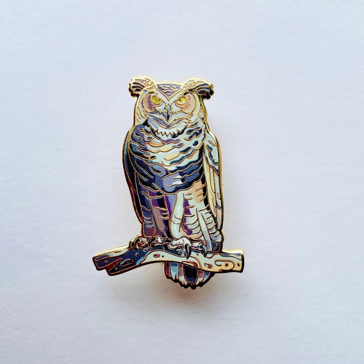An ornate pin depicting an owl, with intricate details and a metallic finish.