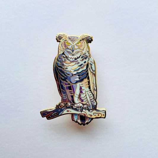 An ornate pin depicting an owl, with intricate details and a metallic finish.