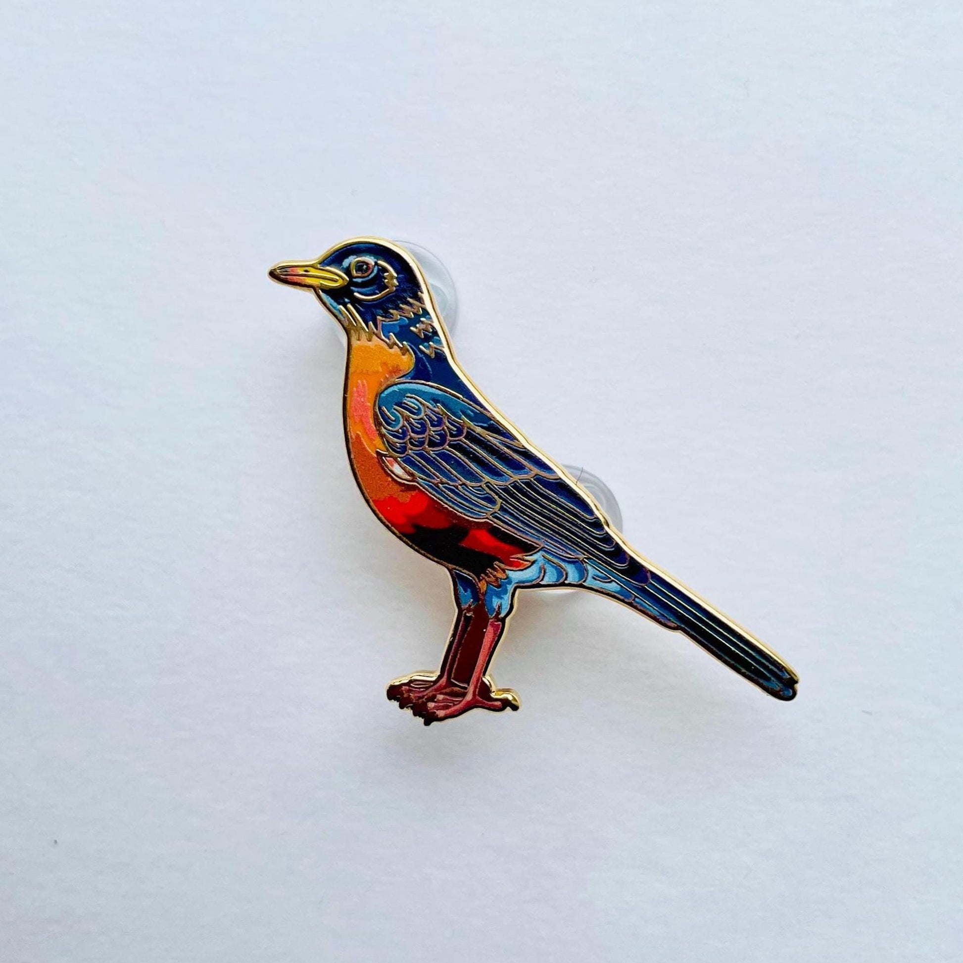 A colorful bird pin is shown against a plain white background.