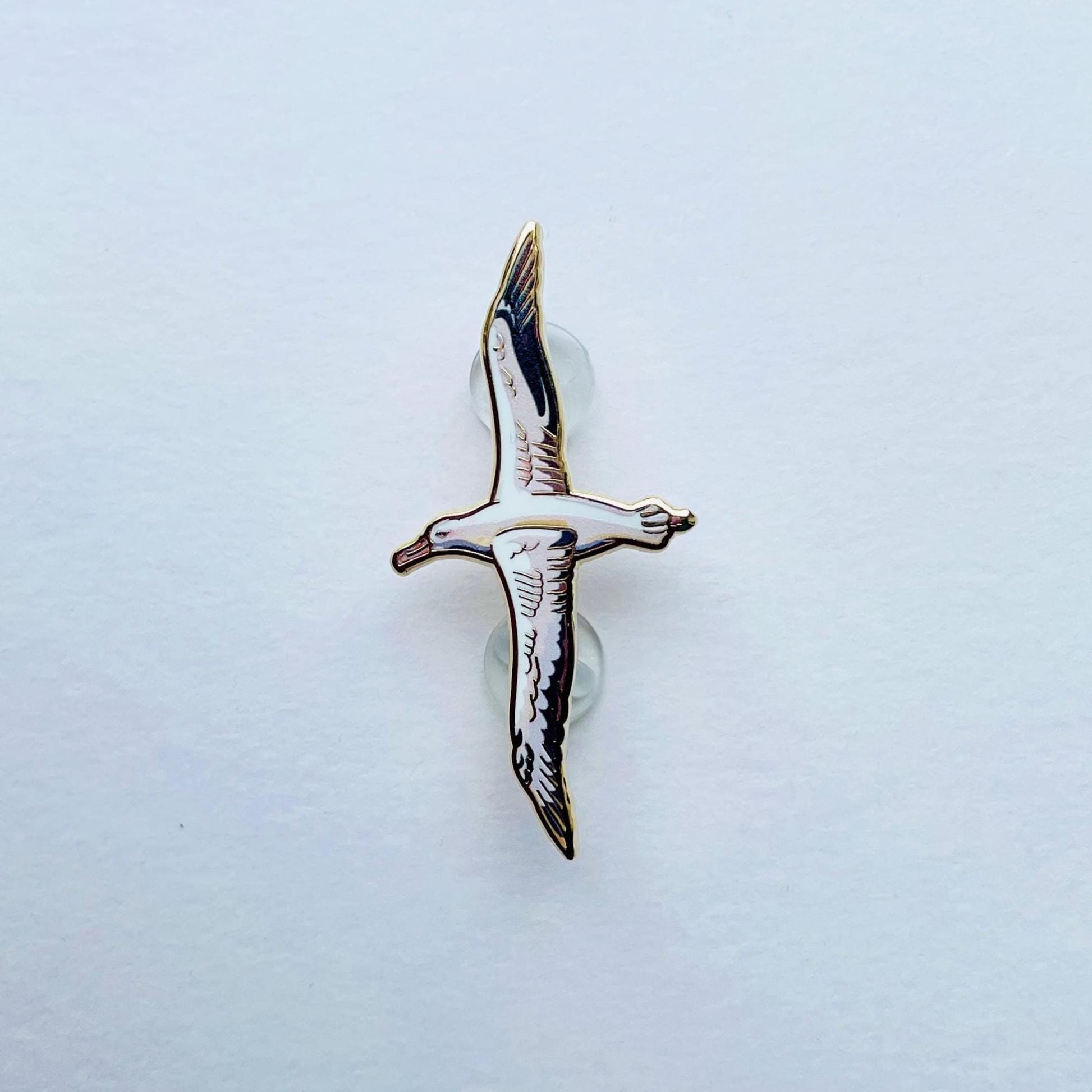 A single, detailed enamel pin depicting a bird in flight against a plain white background.