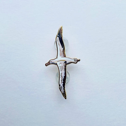 A single, detailed enamel pin depicting a bird in flight against a plain white background.