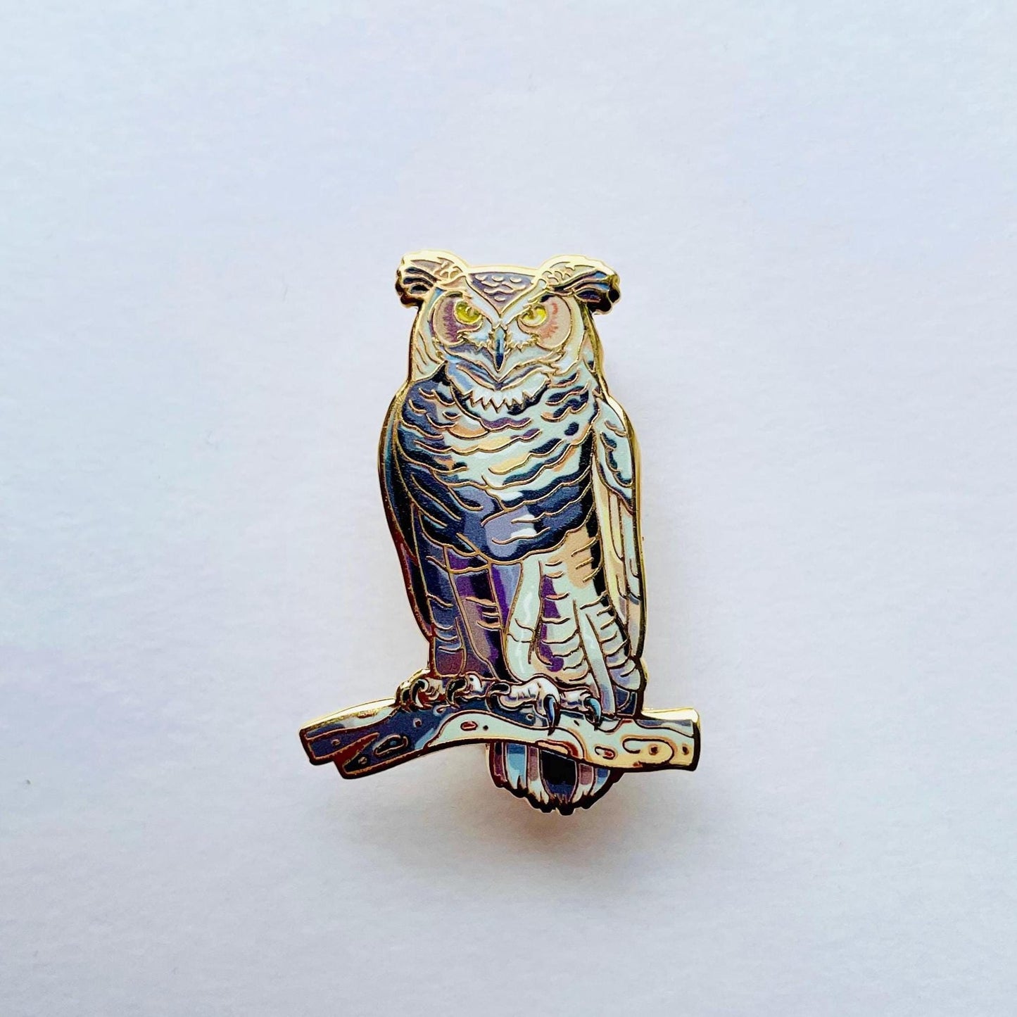 An ornate pin depicting an owl, with intricate details and a metallic finish.