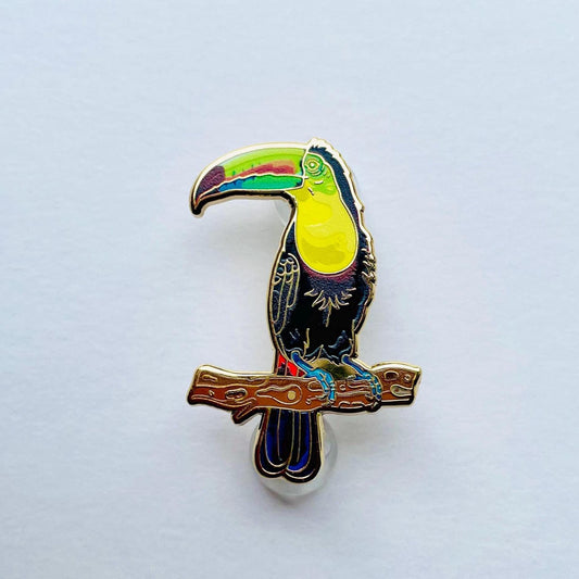 A colorful pin depicting a toucan perched on a branch.