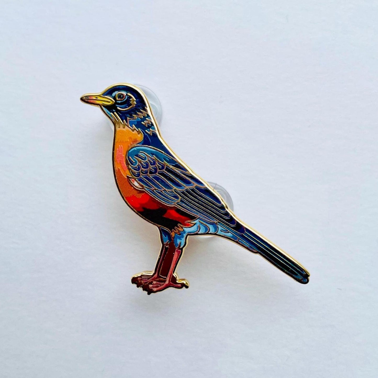 A colorful bird pin is shown against a plain white background.