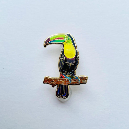 A colorful pin depicting a toucan perched on a branch.