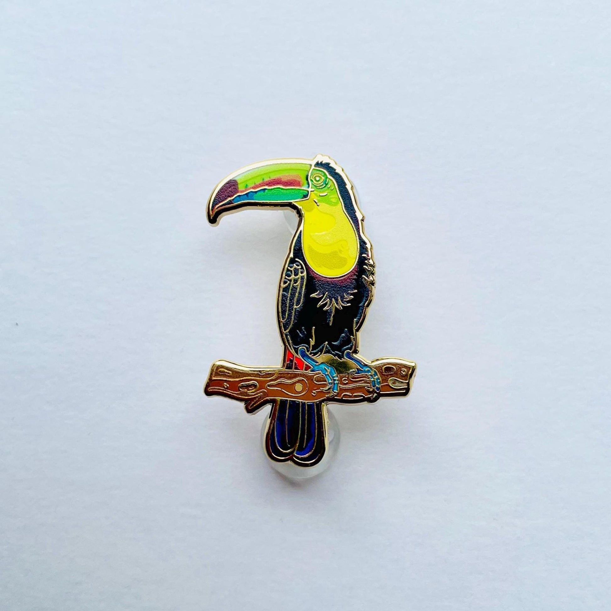 A colorful pin depicting a toucan perched on a branch.