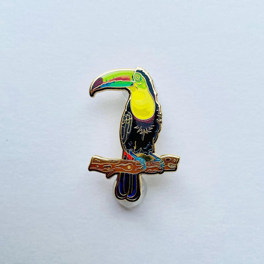 A colorful pin depicting a toucan perched on a branch.