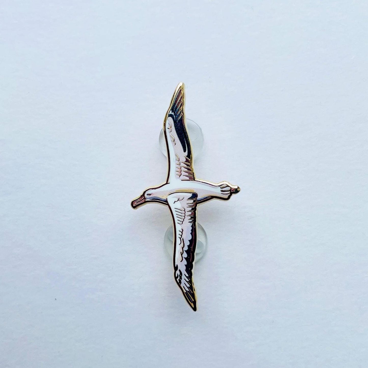 A single, detailed enamel pin depicting a bird in flight against a plain white background.